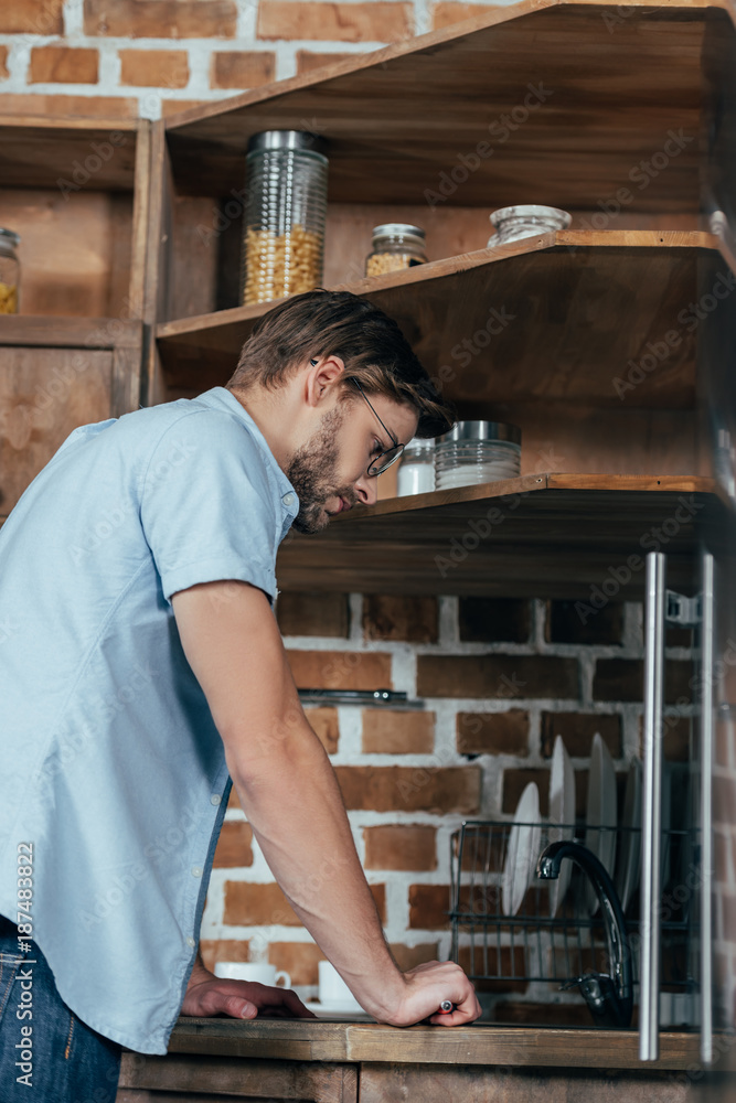side view of casual young man repairing sink in kitchen side view of casual young man repairing sink in kitchen