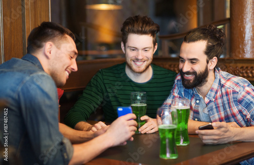 friends with smartphone drinking green beer at pub