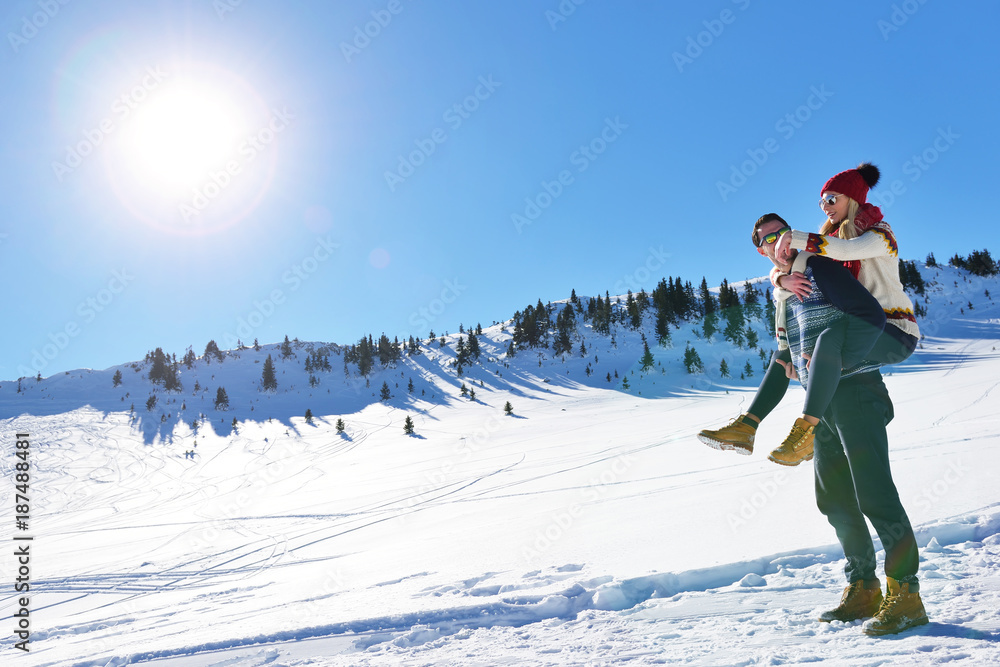 Young couple having fun on snow. Happy man at the mountain giving piggyback ride to his smiling girlfriend.