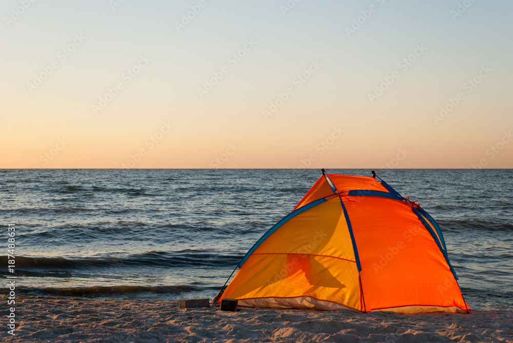 bright orange yellow tent empty, sunrise on the seashore, in the sun, against the blue sea and blue sky, yellow sand, beach, rest, summer