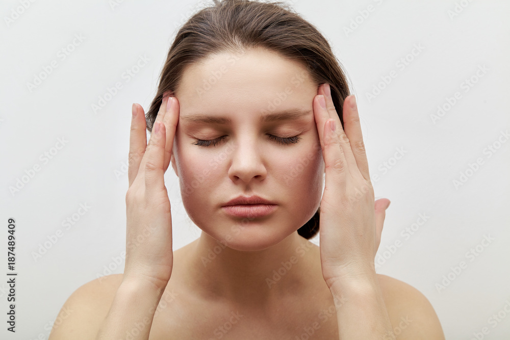 Portrait of young female model with closed eyes making herself facial massage, softly touching her skin applying gentle pressure. Daily beauty routine concept. Portrait of young female model with closed eyes making herself facial massage, softly touching her skin applying gentle pressure. Daily beauty routine concept.