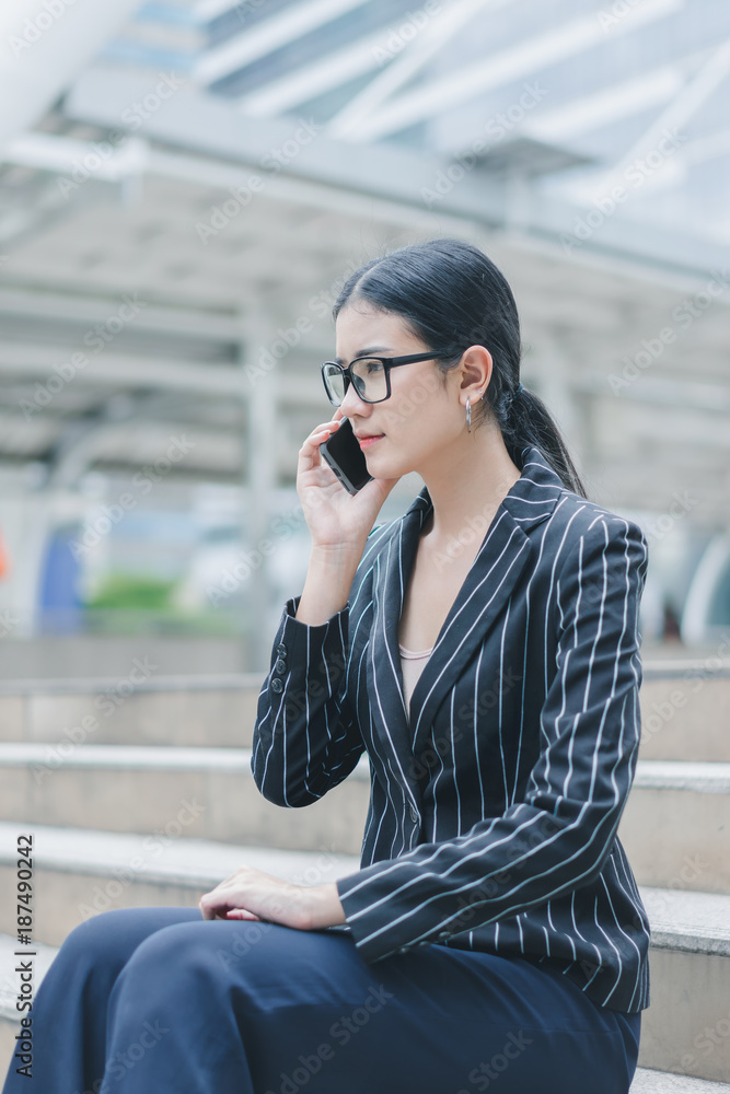 Asian businesswoman is using smartphone while sitting on stair outside office