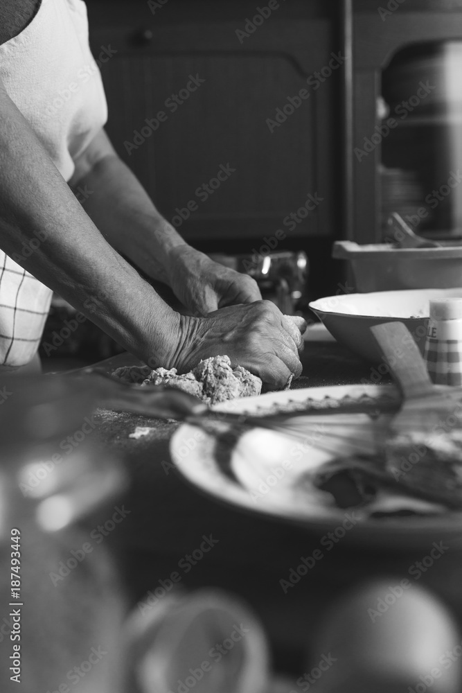 Fototapeta premium Senior female baker kneading dough in kitchen. Black And white.