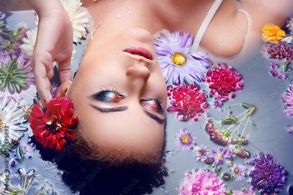 Brunette girl with glamorous makeup and clean the skin in water with flowers close-up top view Brunette girl with glamorous makeup and clean the skin in water with flowers close-up top view