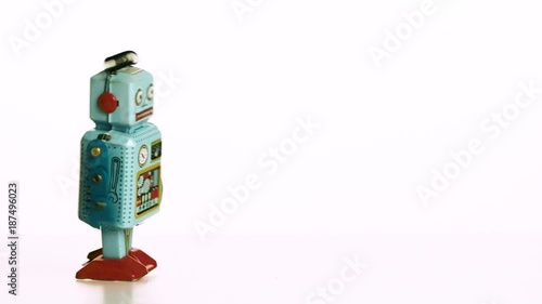 Simple toy robot walking into frame from left side, then running out of energy. White background.