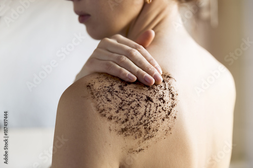 Fotografie, Obraz Beauty, spa and healthy skin concept - woman cleans skin of the body with coffee scrub in bathroom