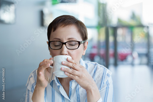 Older woman drinking coffee. Middle aged woman having coffee or tea in a cafe or in the office during coffee break or lunchtime.