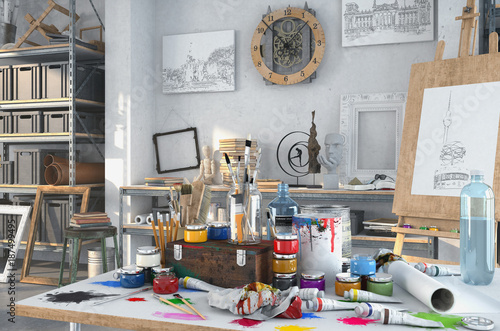 Künstlerische Ausstattung im Atelier mit einem Tisch voller Farben und Pinsel, im Hintergrund Gemälte, Regale und einer Staffelei aus Holz.