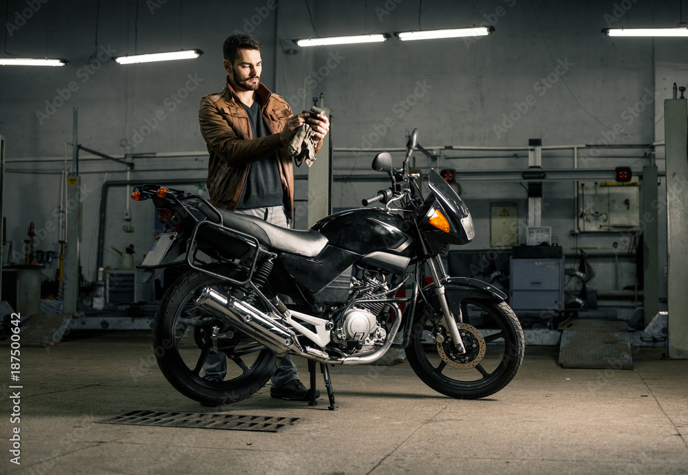 Fototapeta premium Młody człowiek stoi blisko motocyklu w garażu w skórzanej kurtce