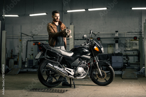 Young man in leather jacket standing near motorcycle in garage