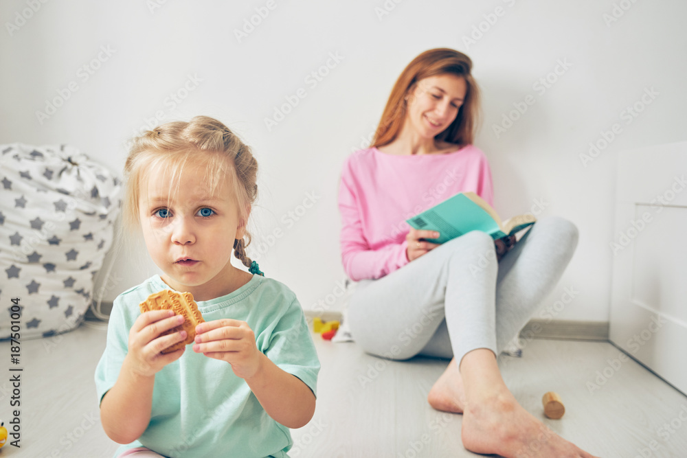 Young mother reading a book to her cute little daughter while sitting on the floor Young mother reading a book to her cute little daughter while sitting on the floor