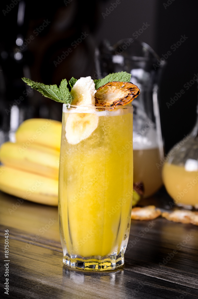Banana alcoholic cocktail with beer, amaretto liqueur, whiskey, vermouth and ice in a glass decorated, black bar background, Closeup