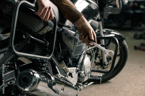 Biker's hands holding wrench near motorcycle
