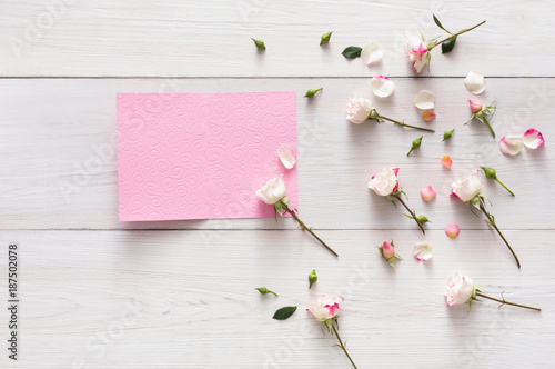 Pink rose flowers and petals on white rustic wood, open empty greeting card