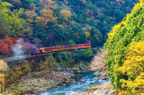 beautiful mountain view in colorful autumn season with sagano scenic railway or romantic train on bridge and boat in the river in Arashiyama, Kyoyo, Japan photo