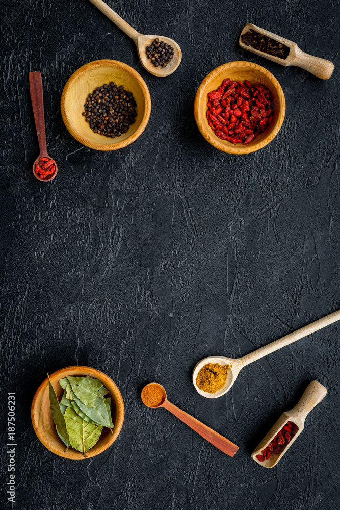 Template for menu design. Empty space near scoops and spoons with spices, bowls with goji, bay leaf, pepper on black background top view Template for menu design. Empty space near scoops and spoons with spices, bowls with goji, bay leaf, pepper on black background top view