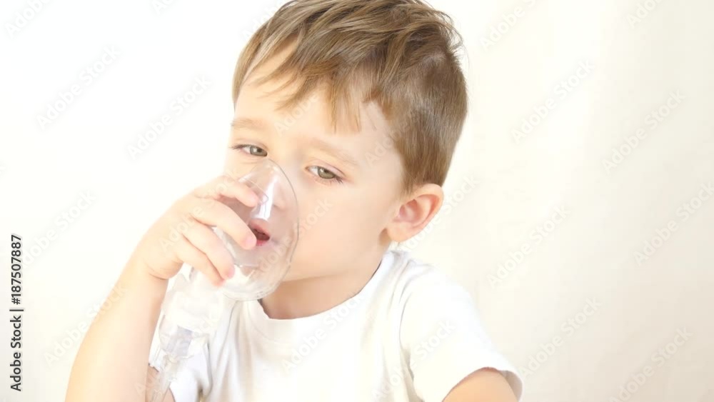 Child breathes through the transparent mask of the inhaler, close-up. The child sits at the table and with pleasure makes inhalation Child breathes through the transparent mask of the inhaler, close-up. The child sits at the table and with pleasure makes inhalation
