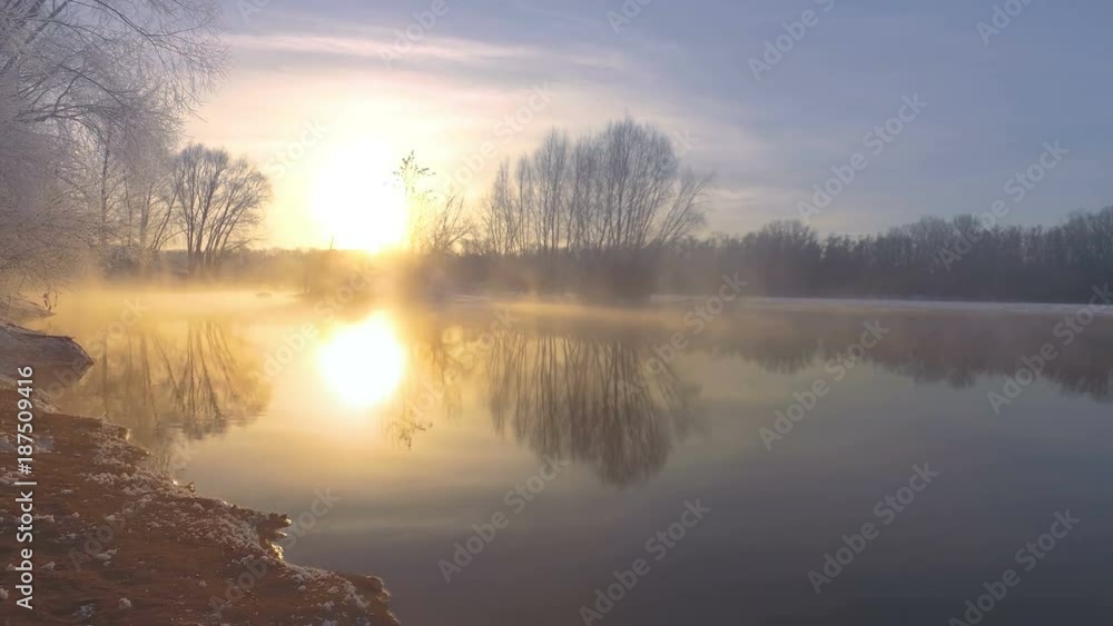 A winter walk along the shore of a hot spring flowing into the river. Frosty morning, beautiful winter landscape with a frozen river, soft light of the rising sun. Nice reflections on water surface. A winter walk along the shore of a hot spring flowing into the river. Frosty morning, beautiful winter landscape with a frozen river, soft light of the rising sun. Nice reflections on water surface.
