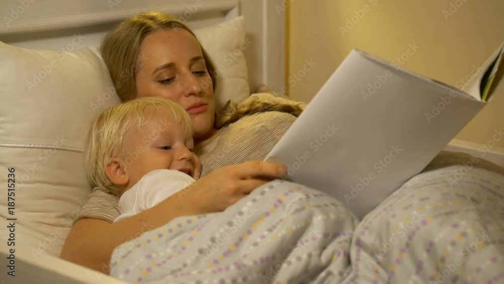 mother and baby son reading a book in bed mother and baby son reading a book in bed