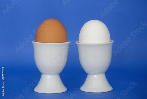 A brown and white egg are shown in egg cups on a blue background