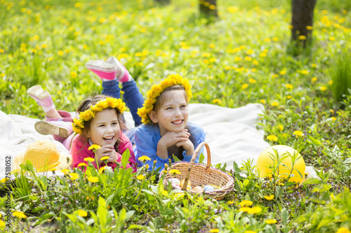 two happy sisters lie on a green meadow with a basket of Easter eggs