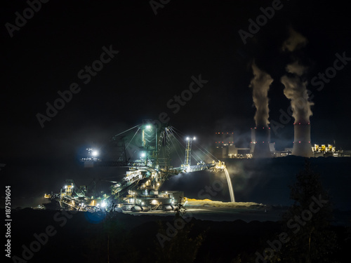 Coal digger opencast mine at night with coal powered power plant in the background
