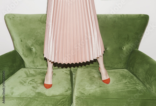 Low section of a woman in pink skirt standing on sofa photo