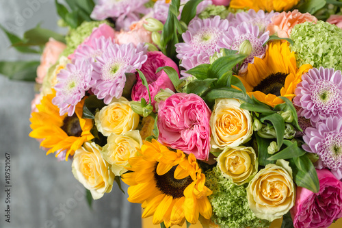 beautiful bouquet of mixed flowers in a vase on wooden table. the work of the florist at a flower shop. a bright mix of sunflowers, chrysanthemums and roses © malkovkosta