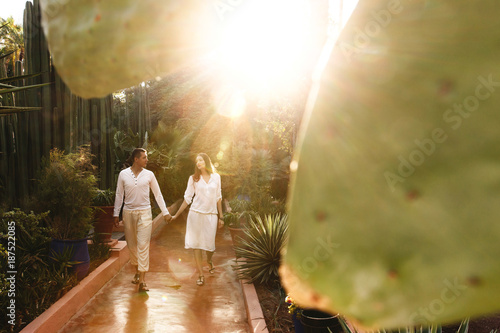 Sun shines over couple in white closes walking around the botanic garden in African city