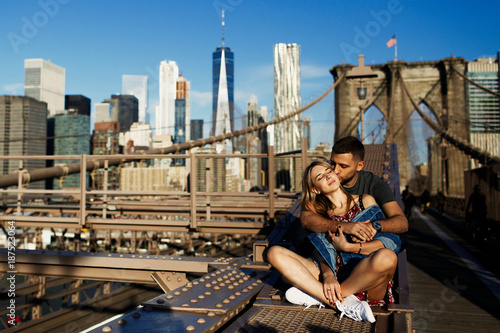 Beautiful young man and woman pose on the Brooklyn Bridge in the rays of morning sun