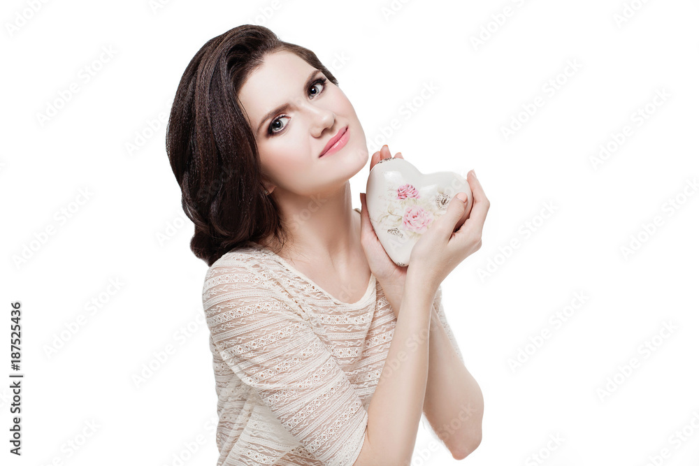 Portrait of beautiful young girl with hairstyle and makeup in beige lace shirt holding ceramic heart with pink flowers isolated on white. Happy Valentine Day. Stylist. Portrait of beautiful young girl with hairstyle and makeup in beige lace shirt holding ceramic heart with pink flowers isolated on white. Happy Valentine Day. Stylist.