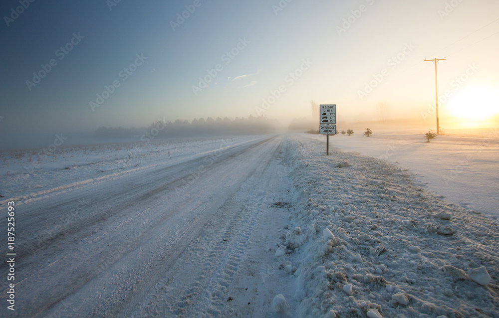 Winter Driving Background. Rural country snow covered road with a frigid winter wind blowing snow across the horizon.