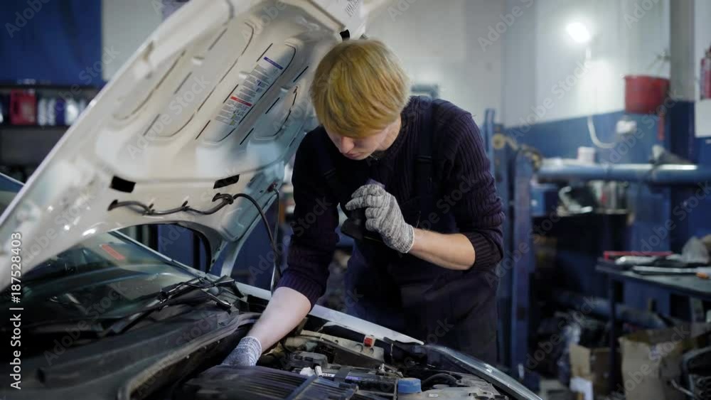 young car mechanic is engaged in repairing the machine with his hands in gloves, the car has a hood young car mechanic is engaged in repairing the machine with his hands in gloves, the car has a hood