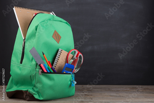 Obraz na plátne Education concept - school backpack with books and other supplies, blackboard ba