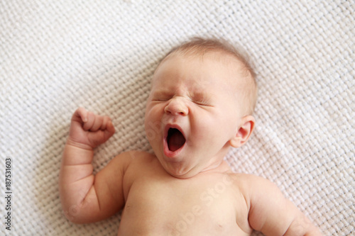 Newborn baby boy yawning while lying on the bed photo