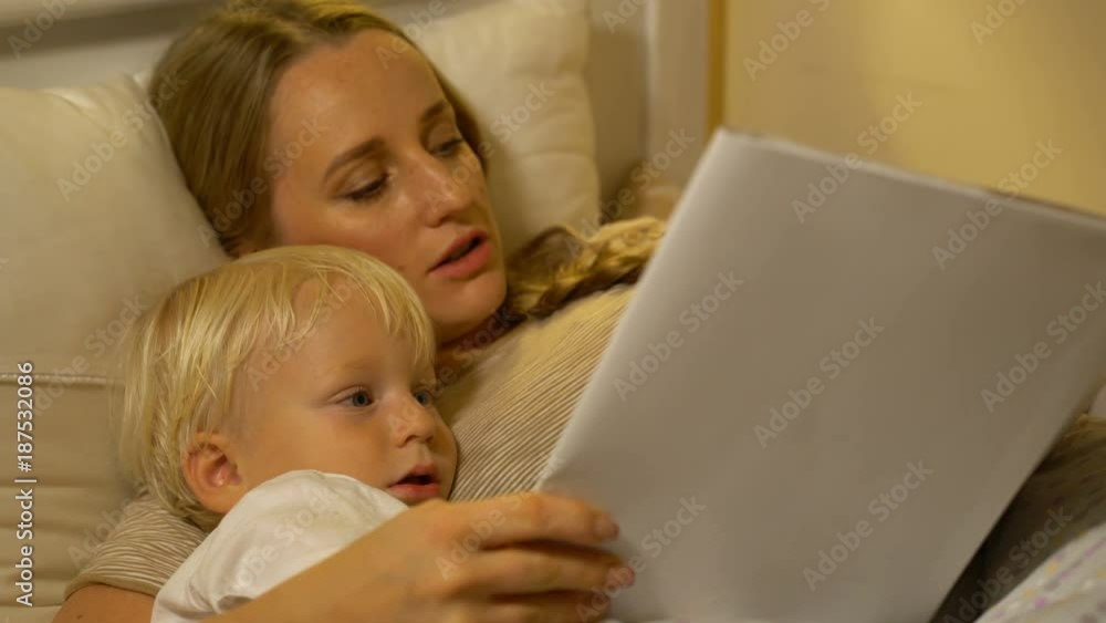 mother and baby son reading a book in bed mother and baby son reading a book in bed