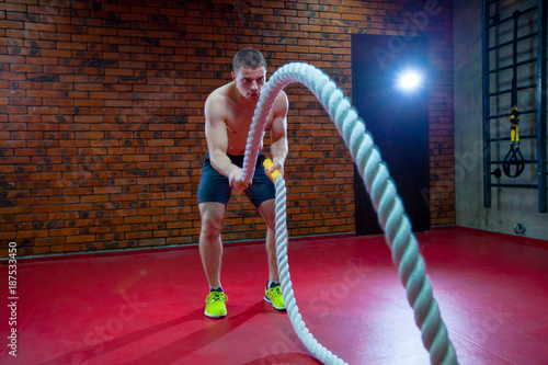 Muscular Shirtless Man in a Gym Exercises with Battle Ropes During His Fitness Workout High-Intensity Interval Training.