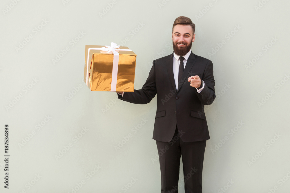 Businessman holding gift box, pointing fingers at camera and smiling