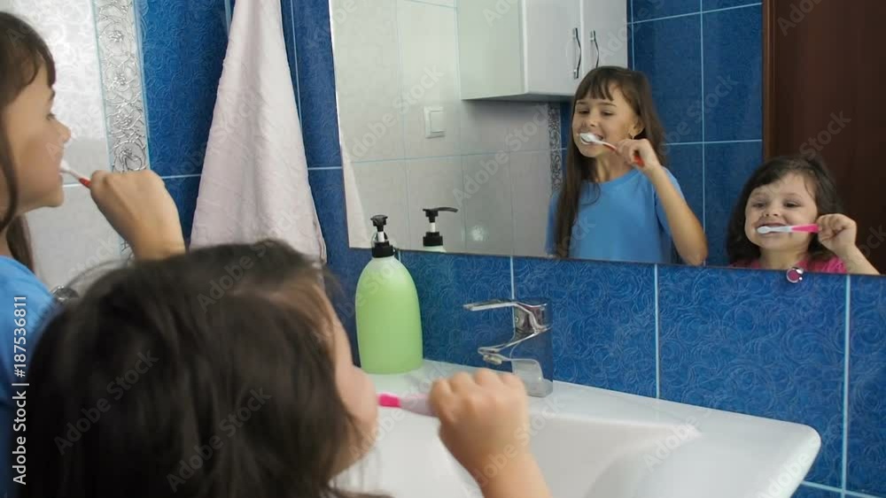 Happy children brush their teeth. Two sisters in front of a mirror brush their teeth. Happy children brush their teeth. Two sisters in front of a mirror brush their teeth.