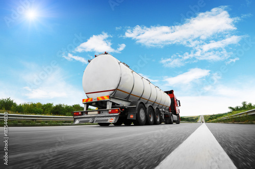 Rear view of big metal fuel tanker truck in motion shipping fuel against sky