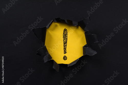 black torn paper revealing exclamation mark on yellow paper. exclamation mark background concept