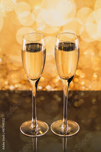 Two glasses of champagne with golden light bokeh on background.