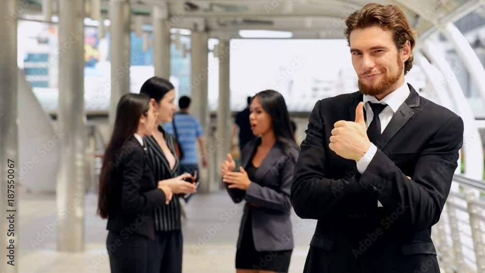 Young business man portrait with his friends in background talking. Thumbs up action. Medium shot. Success business project. Young business man portrait with his friends in background talking. Thumbs up action. Medium shot. Success business project.