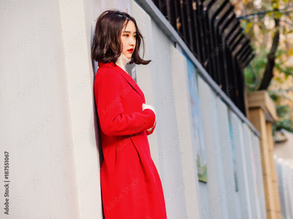 Fototapeta premium Beautiful young brunette woman wearing a red coat in autumn city. Outdoor fashion portrait of glamour young Chinese cheerful stylish lady in street. Emotions, people, beauty and lifestyle concept.