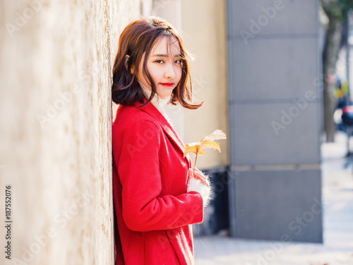 Beautiful young brunette woman wearing a red coat in autumn city. Outdoor fashion portrait of glamour young Chinese cheerful stylish lady in street. Emotions, people, beauty and lifestyle concept. © atiger