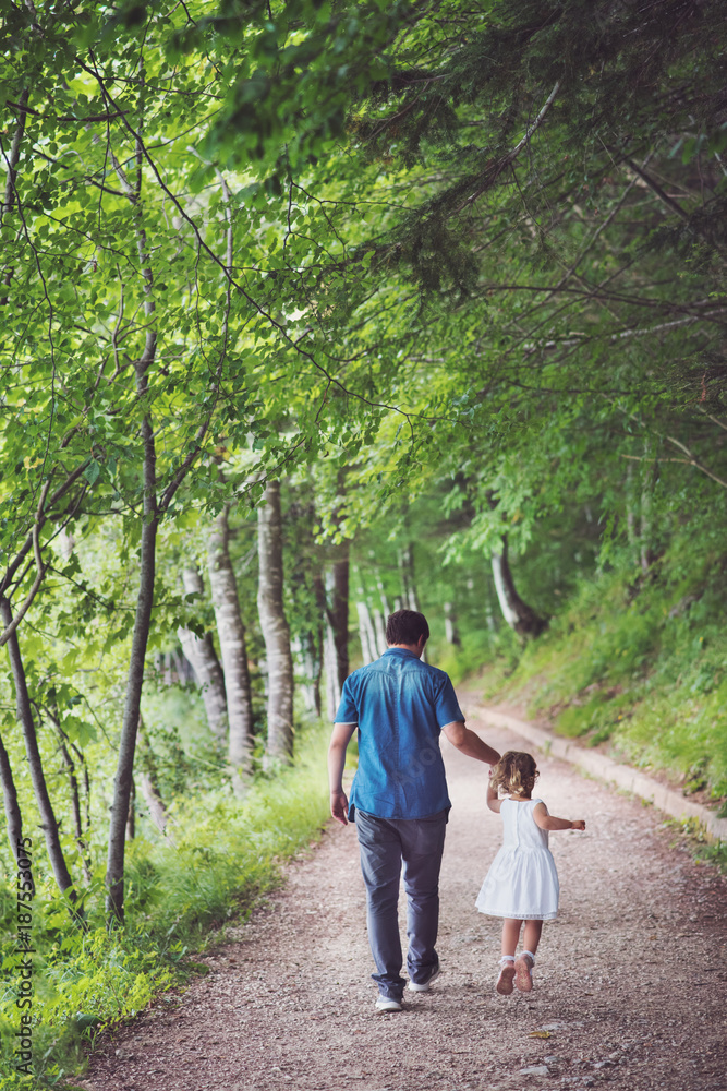 Father and daughter walking in a park among trees Father and daughter walking in a park among trees