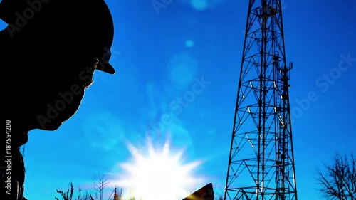 Silhouette engineer working on digital tablet, with satellite dish telecom network on telecommunication tower in sunset. photo