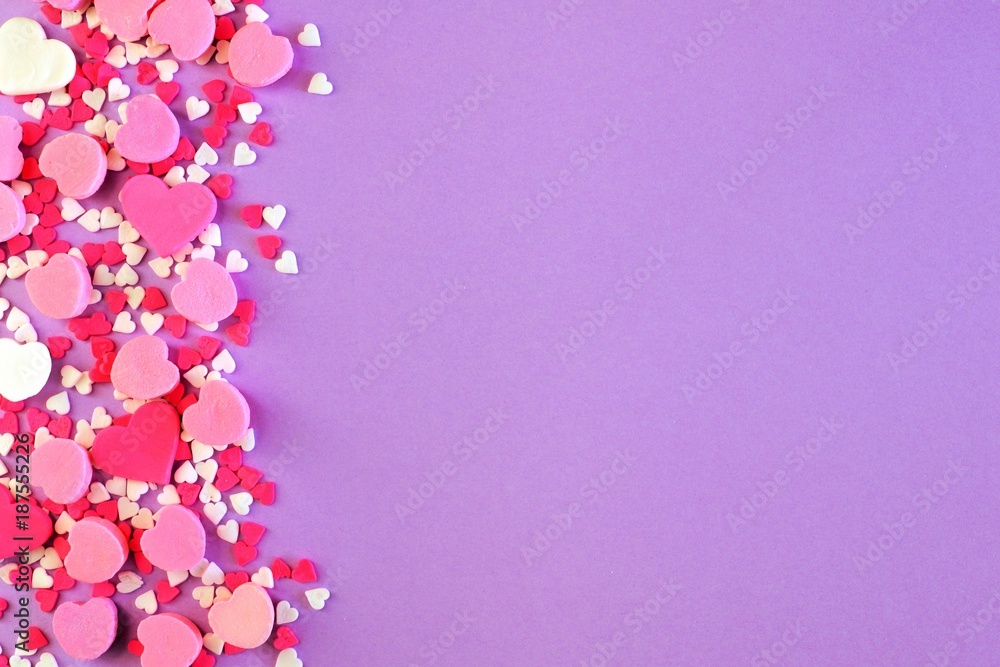 Side border of assorted Valentines Day sweets and candy over a pastel purple background