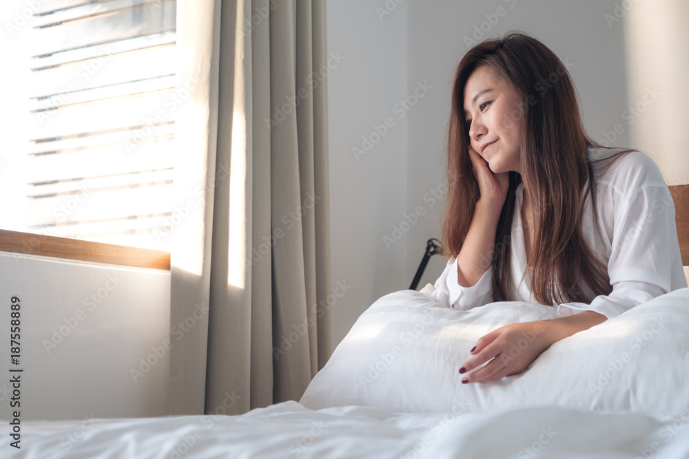 Portrait image of a beautiful Asian woman sitting on the bed after woke up with feeling happy and relaxed Portrait image of a beautiful Asian woman sitting on the bed after woke up with feeling happy and relaxed