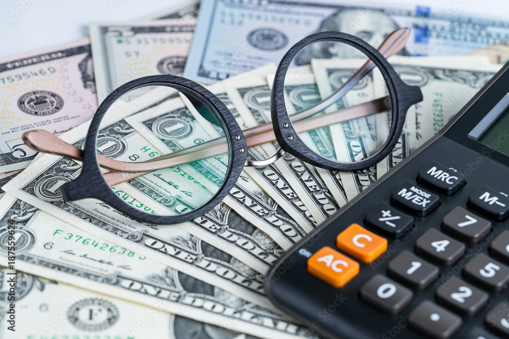 Business accounting or tax calculation concept with glasses on pile of dollar banknotes and calculator on the table Business accounting or tax calculation concept with glasses on pile of dollar banknotes and calculator on the table